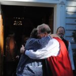 Archbishop Fred Hiltz hugs Canon Ginny Doctor, Indigenous ministries co-ordinator for the Anglican Church of Canada, following the Mohawk Chapel service. National Indigenous Anglican Bishop Mark MacDonald watches over Hiltz' shoulder. Photo: André Forget