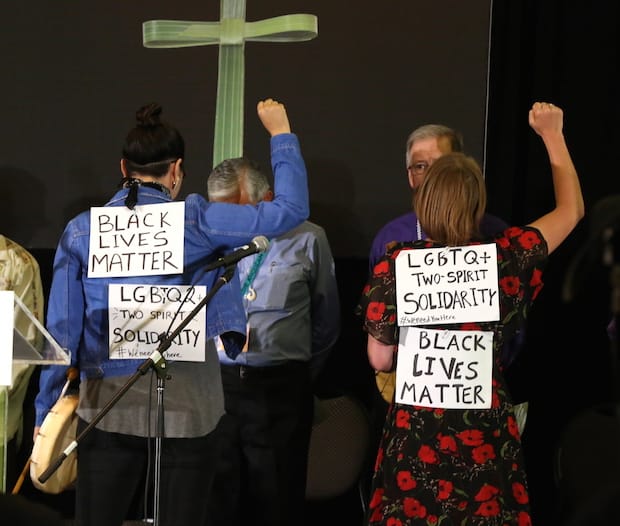 Danielle Black and The Rev. Leigh Kern raise fists onstage and show handwritten signs fastened to their tops, expressing support for LGBTQ + Two Spirit and the Black Lives Matter movement. Photo: Art Babych 