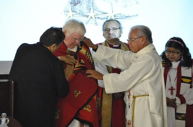 Former indigenous ministries co-ordinators Donna Bomberry and The Rev. Canon Laverne Jacobs wrap “The Evening Star” Pendleton blanket over Archbishop Michael Peers as Bishops Adam Halkett and Lydia Mamakwa look on. Photo: Marites N. Sison